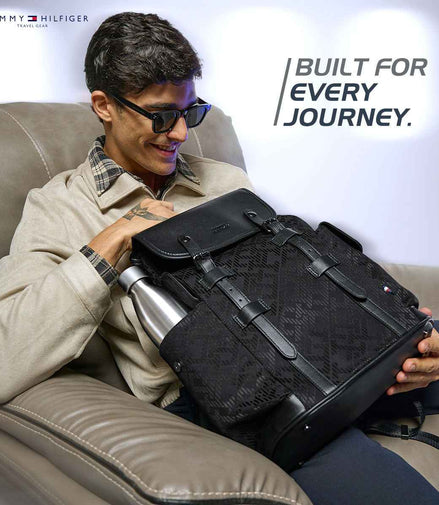 Tommy Hilfiger Alden Flap-Top Laptop Backpack in Black — lifestyle shot, model with the backpack on a sofa